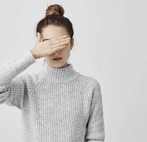 Mujer con un suéter gris cubriéndose los ojos con la mano, ilustrando el concepto de accesibilidad web.