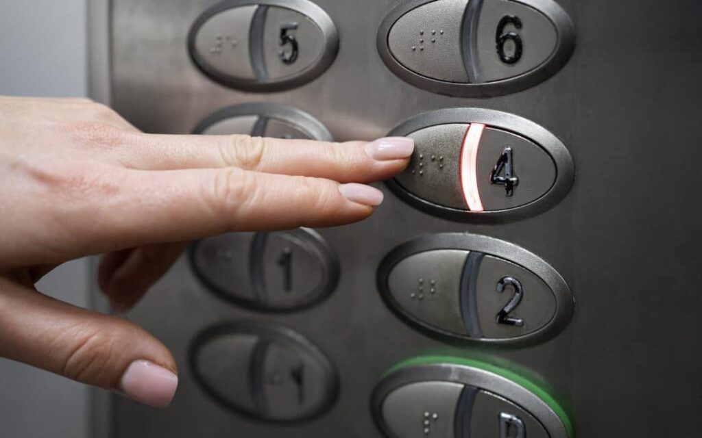 Una persona presionando con el dedo el botón número cuatro en un panel de control de ascensor, considerando los tipos de discapacidades y su accesibilidad web.