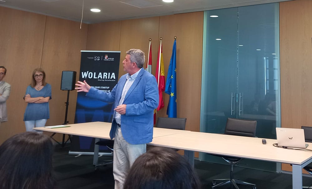 Hombre dando una presentación sobre AccedeMe proyecto escogido por WOLARIA en una sala de conferencias con oyentes y un fondo de marca.