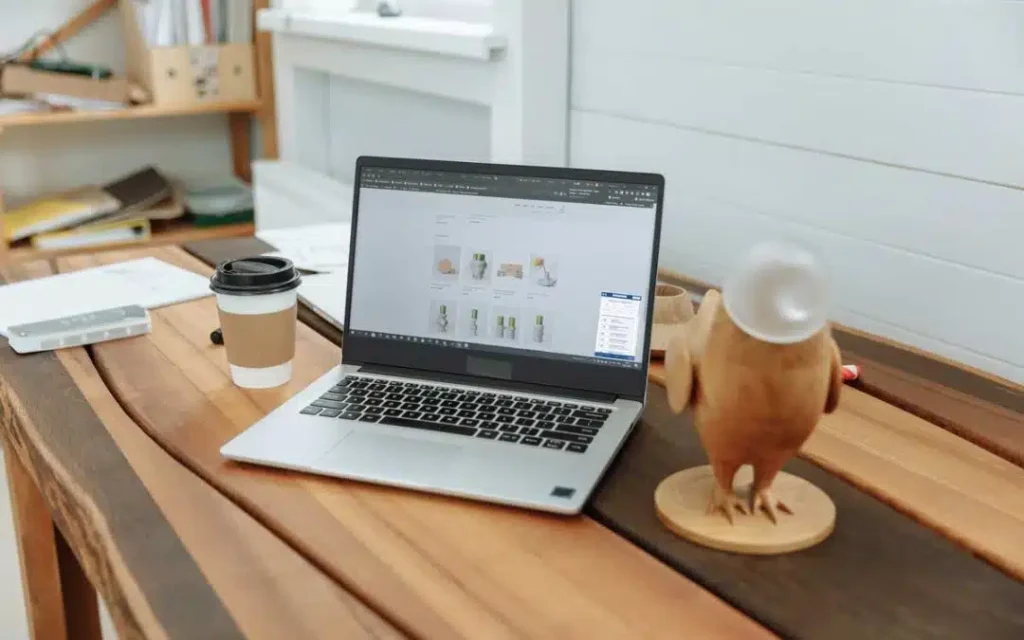 Una computadora portátil abierta en un sitio web de comercio electrónico, discutiendo Ventajas y beneficios sobre la Accesibilidad Web, junto a una taza de café y una escultura de un pájaro de madera sobre una mesa.