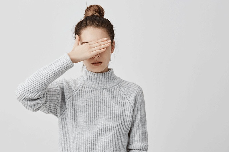 Mujer con un suéter blanco cubriéndose los ojos con la mano, simbolizando la importancia de la accesibilidad web.